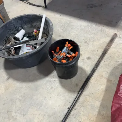 Sale Photo Thumbnail #53: Collection of workshop tools and supplies, including a bucket filled with spring clamps, a wash tub of miscellaneous hardware, and a long metal bar.