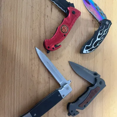 Sale Photo Thumbnail #146: Collection of four modern folding pocket knives, including a red Fire Fighter themed knife, a rainbow titanium finish blade with flame-pattern handle, a SOG tactical knife, and a classic-style lockback.