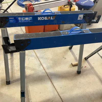 Sale Photo Thumbnail #34: Pair of blue Kobalt folding metal sawhorses featuring built-in carrying handles and non-skid tops, showing light surface wear.
