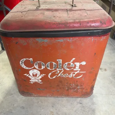 Sale Photo Thumbnail #168: Vintage metal Cooler Chest portable ice chest featuring a red finish and bail handle, showing significant distressing, rust, and paint wear.