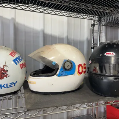 Sale Photo Thumbnail #24: Trio of vintage racing helmets, including two white helmets with decals and one matte black Bell full-face helmet.