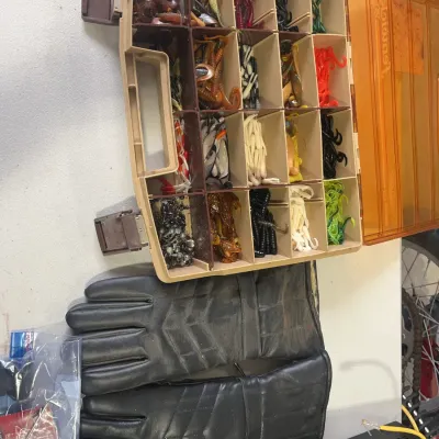 Sale Photo Thumbnail #159: Open Fenwick tackle box filled with soft plastic fishing lures and terminal tackle alongside a pair of black leather work gloves.