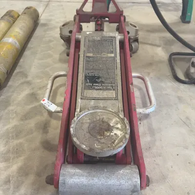 Sale Photo Thumbnail #73: A 2-ton (4,000 lb) capacity hydraulic floor jack with red frame, aluminum lift body, and side carry handles, showing heavy surface wear.