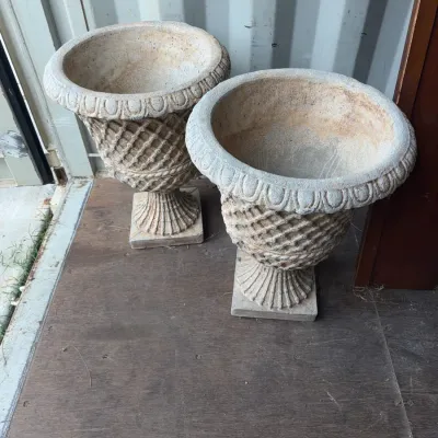 Sale Photo Thumbnail #103: Pair of stone urn planters featuring a crosshatch pattern, egg-and-dart rim detail, and square bases with a weathered patina.