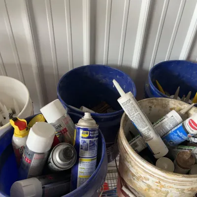 Sale Photo Thumbnail #21: Assorted workshop chemicals and supplies, including spray paint, WD-40, and caulk tubes organized in plastic buckets.