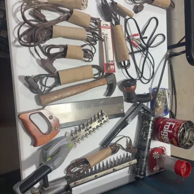 Sale Photo Thumbnail #89: Assortment of household hand tools and supplies, including extension cords wrapped in cardboard sleeves, a claw hammer, hand saw, grease gun, and electric hedge trimmer.