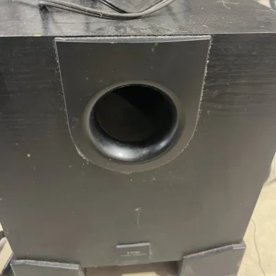 Sale Photo Thumbnail #175: Black wooden powered subwoofer speaker with a front bass port and attached power cord, showing light surface dust and wear.