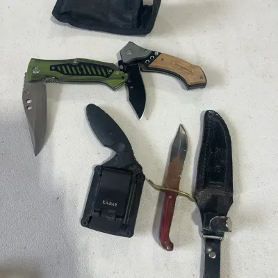 Sale Photo Thumbnail #150: Collection of modern tactical and hunting knives, including folding pocket knives, a KA-BAR sheath knife, and a rusted fixed-blade knife with a brass crossguard.