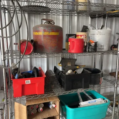 Sale Photo Thumbnail #23: Wire shelving unit holding various garage supplies, including a vintage red gas can, plastic storage bins, paint filters, and caulking tubes.