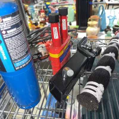 Sale Photo Thumbnail #216: Assorted garage and workshop items including a propane cylinder, STP oil additives, a trailer hitch ball mount, and a horsehair duster brush arranged on a wire rack.