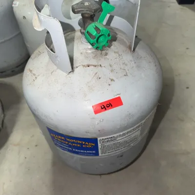 Sale Photo Thumbnail #177: Ozark Mountain Propane Co. 20 lb propane cylinder featuring a safety valve guard and green plastic nozzle cover, showing light surface grime.