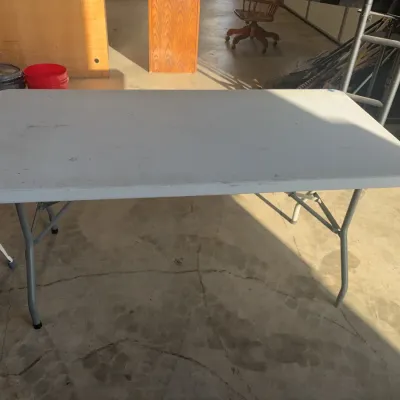 Sale Photo Thumbnail #82: White plastic folding utility table with metal legs, showing light surface wear.
