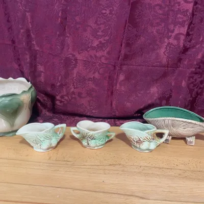 Sale Photo Thumbnail #130: Collection of vintage art pottery planters and dishes, featuring green glazed floral and leaf motifs alongside an mid-century leaf-shaped cornucopia boat planter.