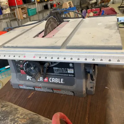 Sale Photo Thumbnail #40: Porter-Cable portable benchtop table saw model PCB22215 resting on a wooden workbench, showing light wear from use.