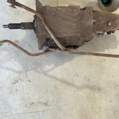 Sale Photo Thumbnail #37: Vintage manual vehicle transmission assembly with attached shift linkages, showing surface dirt and rust from storage.