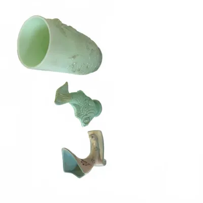 Sale Photo Thumbnail #290: Collection of three light green ceramic pieces including a floral vessel, a molded fish figurine, and a curved decorative form.