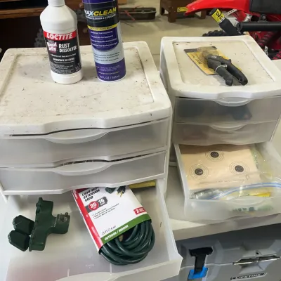 Sale Photo Thumbnail #157: Two white plastic three-drawer storage carts containing workshop items, including a light-duty extension cord, paper target sheets, pruning shears, Loctite Rust Dissolver, and Royal Purple Max-Clean fuel system cleaner.