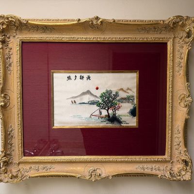 Chinese silk embroidery art depicting a landscape scene, housed in an ornate gilded frame with a burgundy mat.