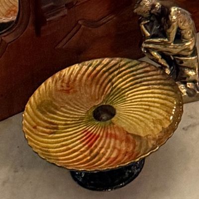 Vintage iridescent glass pedestal bowl with swirl pattern, shown alongside a small brass Thinker sculpture on a marble surface.