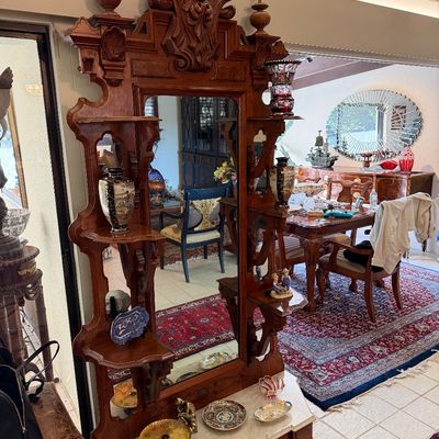 Ornate Victorian carved wood hall tree featuring an asymmetrical mirror, multi-tiered display shelves, elaborate scrollwork cresting, and...