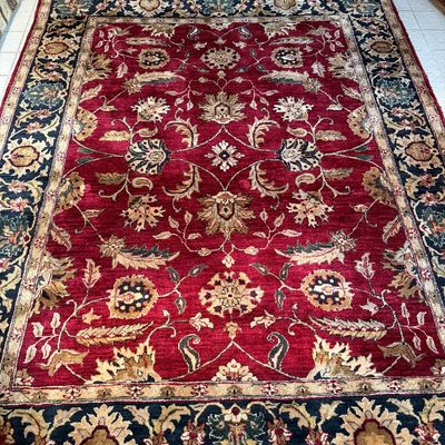 Large traditional-style area rug featuring a rich red field with intricate floral palmettes and a dark navy blue decorative border.