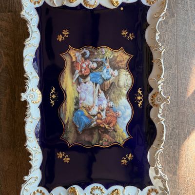 Ornate porcelain serving tray in Rococo style featuring a cobalt blue ground, gilt handles, molded white-and-gold scrollwork rim, and a...