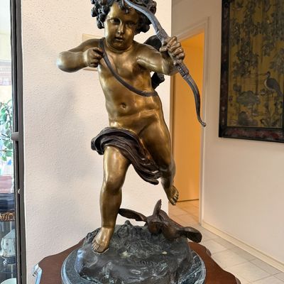 Classical style bronze sculpture of Cupid drawing a bow after Jean-Antoine Houdon, set on a round green marble base.