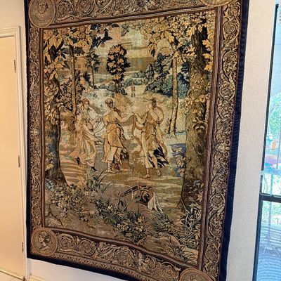 Large woven wall tapestry featuring a classical pastoral scene with three women dancing, framed by an ornate decorative border with...