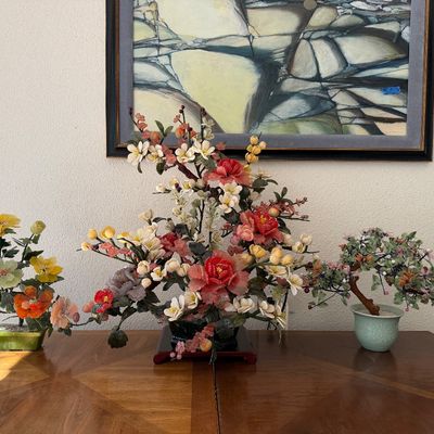 Collection of three Chinese carved glass and gemstone floral bonsai trees arranged on a wooden tabletop, displayed beneath a framed...