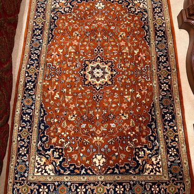 Hand-knotted Persian-style area rug featuring a rust-orange field, central star medallion, intricate floral vines, and navy blue...