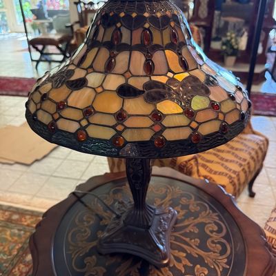 Tiffany-style stained glass table lamp featuring a bell-shaped shade with amber cabochon accents and an ornate dark metal base.
