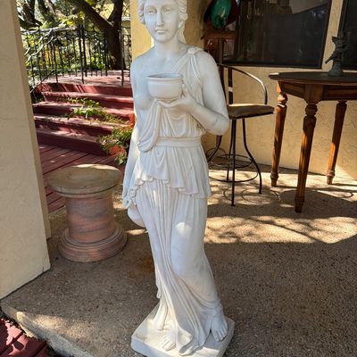 Classical neoclassical white marble or composite garden statue of a draped woman holding a small bowl.