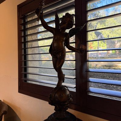 Classical-style bronze statue of a winged cherub holding a torch, standing atop a globe mounted on a dark pedestal.