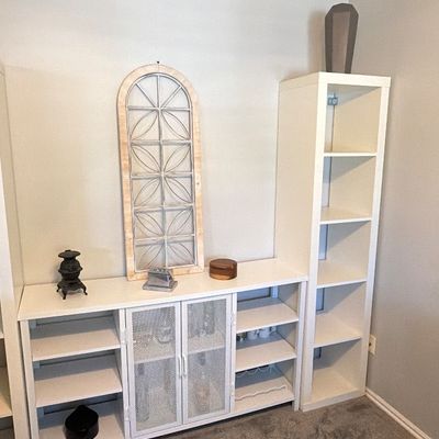 White wooden entertainment media unit with mesh-front cabinets, flanking shelf tower, and decorative accent pieces.