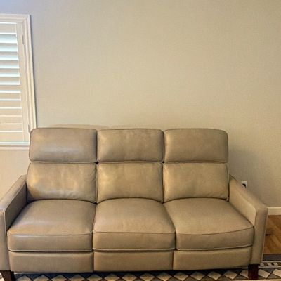 Contemporary beige leather three-cushion reclining sofa with high backs and dark wood feet.