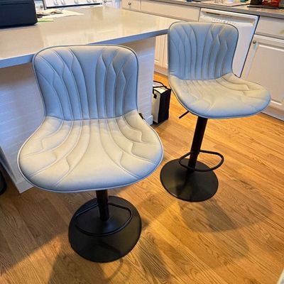 Pair of modern light gray faux leather bar stools featuring channel-stitched contoured seats, adjustable height swivel mechanisms, and...
