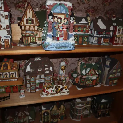 Sale Photo Thumbnail #9: Collection of porcelain and resin Christmas village buildings and figurines displayed on wooden shelves.