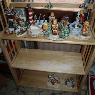 Sale Photo Thumbnail #41: Collection of decorative porcelain figurines and small knick-knacks arranged on a light wood three-tier folding bookshelf.