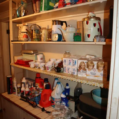 Sale Photo Thumbnail #143: Pantry shelving unit stocked with vintage housewares, teacups, teapot, hair dye boxes, cleaning supplies, and small appliances.