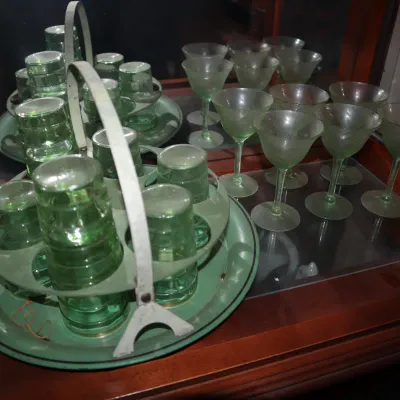 Sale Photo Thumbnail #118: Vintage green glass beverage sets, including drinking glasses in metal caddy carriers and matching frosted stemware inside a wooden display cabinet.