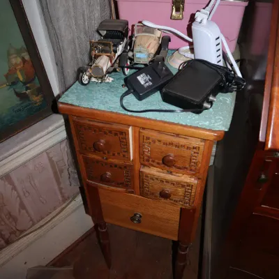 Sale Photo Thumbnail #96: Vintage small wooden cabinet with carved drawer fronts, topped with antique-style model cars, power adapters, and a pink sewing box.