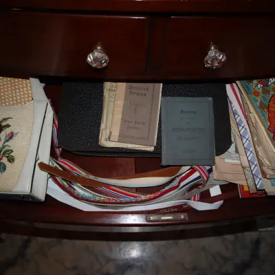 Sale Photo Thumbnail #48: Open wooden dresser drawer containing a vintage needlepoint handbag, small hymn books, striped belts, and various ephemera and papers.