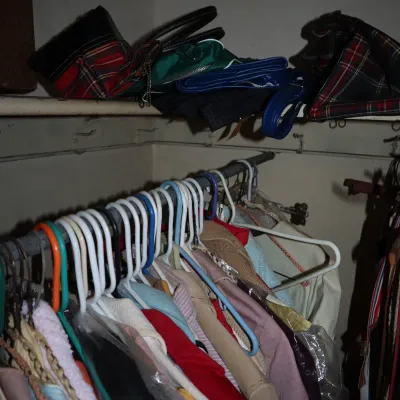 Sale Photo Thumbnail #156: Closet full of vintage women's clothing on plastic hangers with plaid and solid-colored handbags stored on the shelf above.