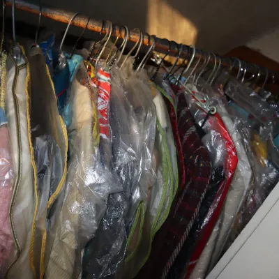 Sale Photo Thumbnail #23: Closet rod filled with vintage clothing items protected in plastic dry cleaning bags and garment covers.