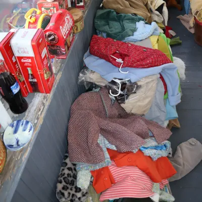 Sale Photo Thumbnail #176: Assorted vintage clothing items stacked along a hallway floor, alongside a shelf filled with Coca-Cola memorabilia.