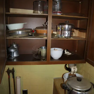 Sale Photo Thumbnail #136: Open wooden kitchen cabinet filled with vintage cookware, glass canisters, mixing bowls, and small appliances including an electric pressure cooker and stand mixer.