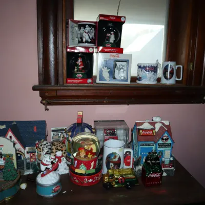 Sale Photo Thumbnail #167: Collection of Coca-Cola Christmas collectibles, including snow globes, ceramic village houses, holiday mugs, and animated figurines.