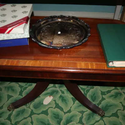 Sale Photo Thumbnail #64: Duncan Phyfe style mahogany coffee table with brass claw feet, featuring boxed Royal Doulton items, a silver-tone serving platter, and a green binder on top.