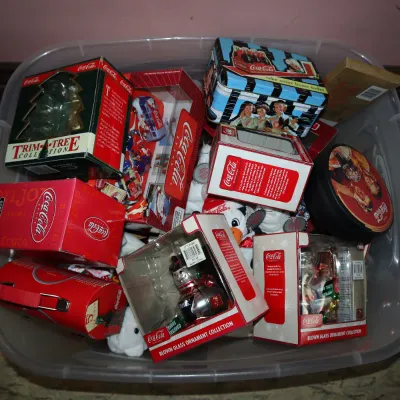 Sale Photo Thumbnail #164: Large clear plastic storage tub filled with Coca-Cola collectibles, including boxed blown glass ornaments, tin containers, plush polar bears, and holiday decor.