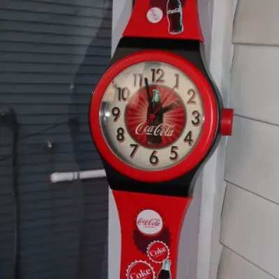 Sale Photo Thumbnail #170: Vintage Coca-Cola giant wristwatch wall clock featuring red straps decorated with bottle cap and contour bottle graphics.